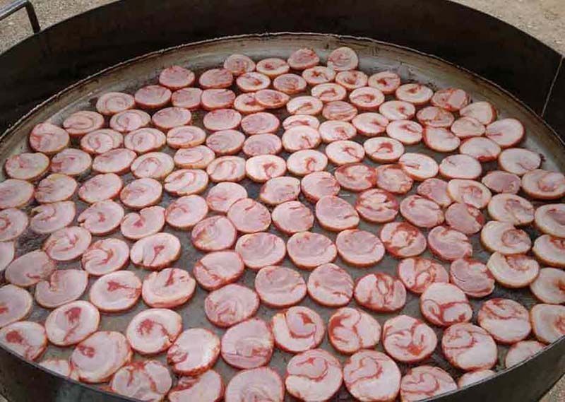 En el suelo hay una gran sartén llena de rodajas de salchicha.