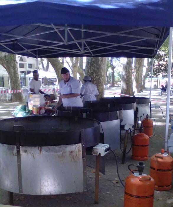 Un grupo de personas cocinando al aire libre bajo una carpa azul.