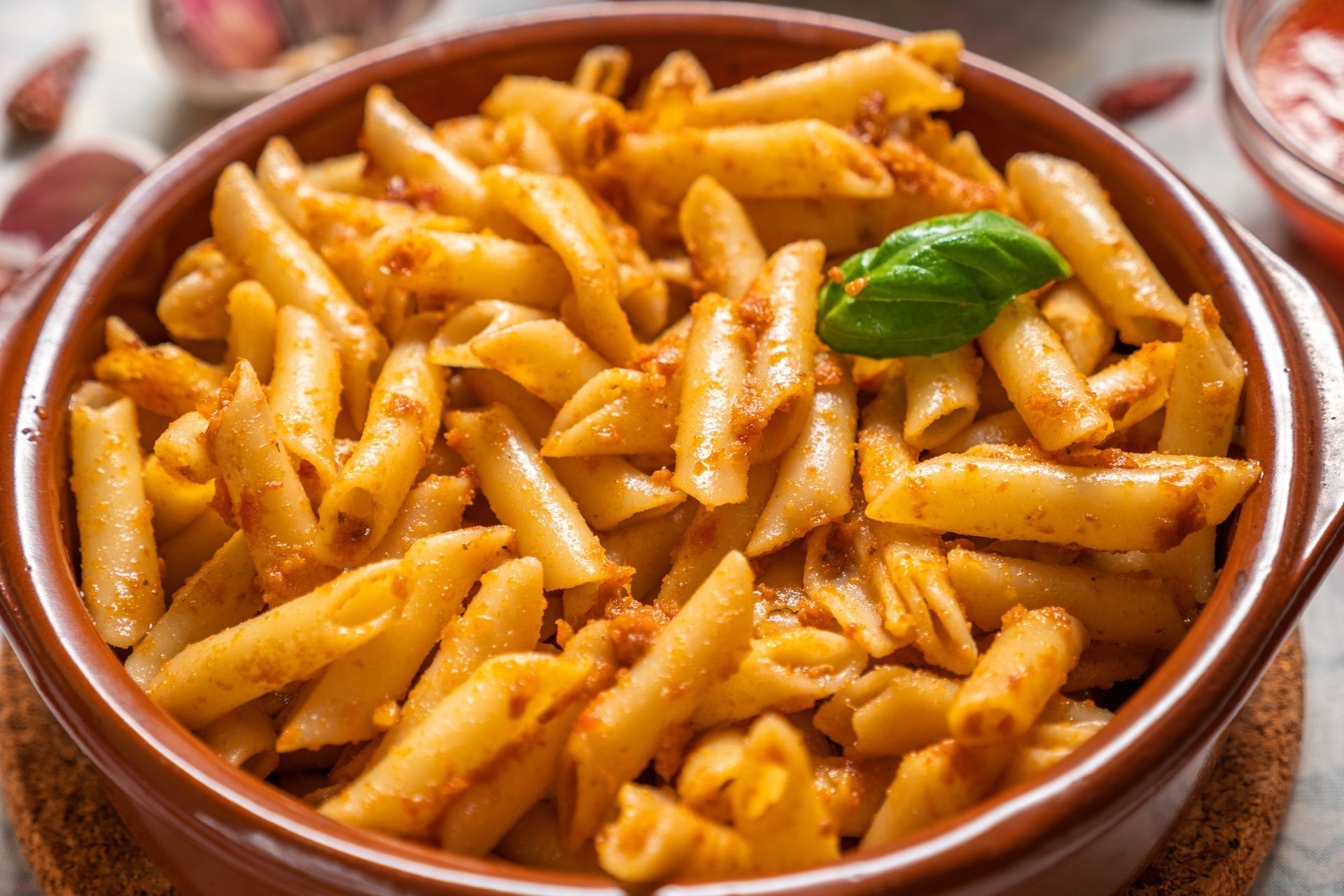 Plato de pasta penne con salsa roja, adornado con albahaca.