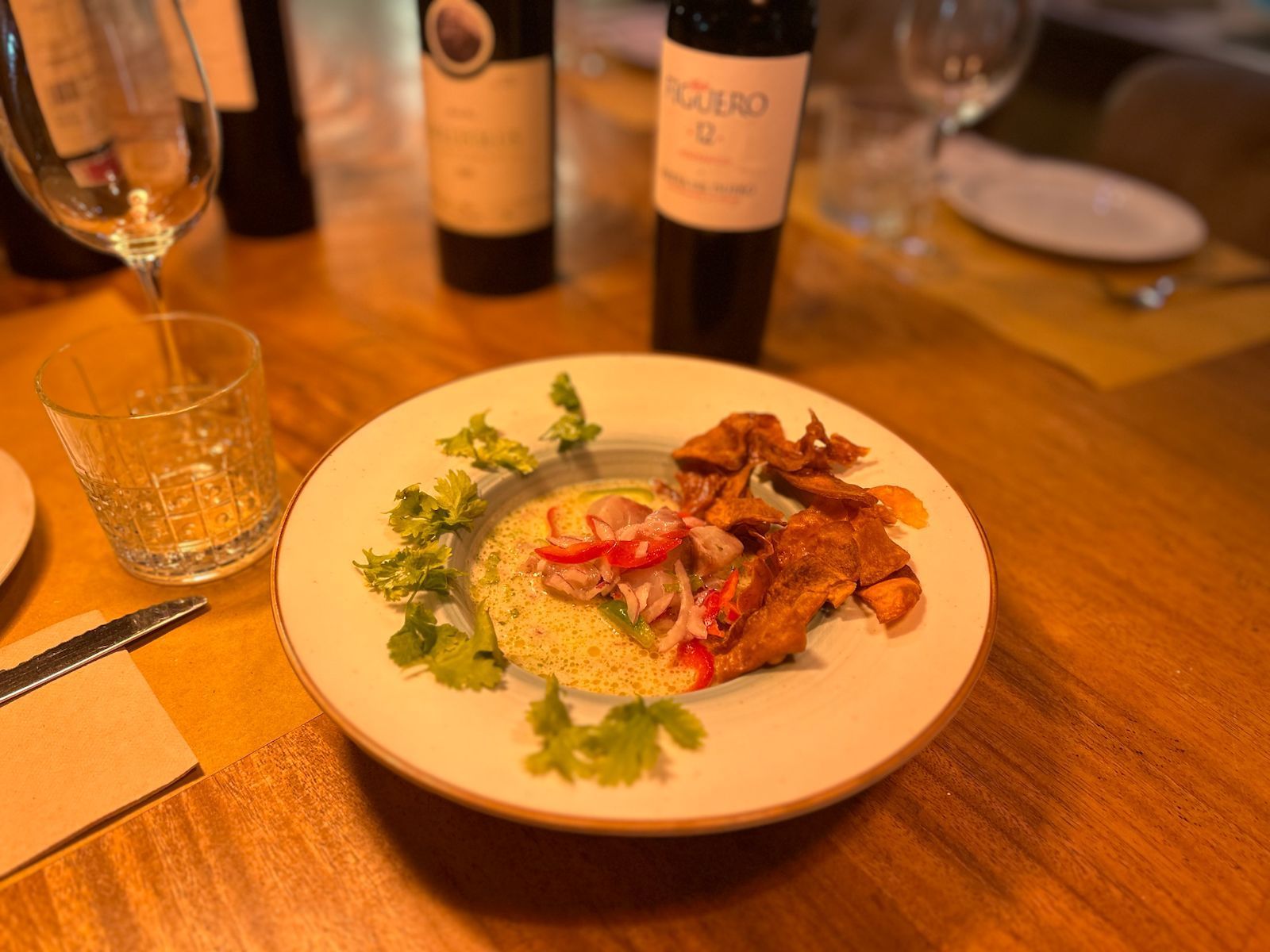 Plato de comida con carne frita, cuscús y cilantro, con botellas de vino de fondo.