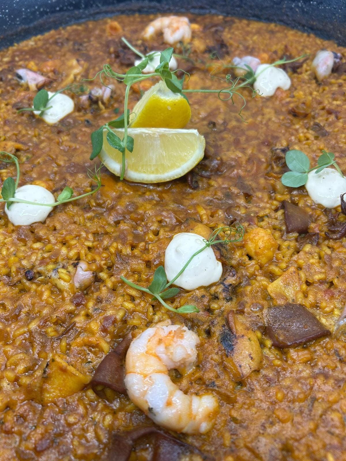 Paella con camarones, rodaja de limón y guarnición de hierbas.
