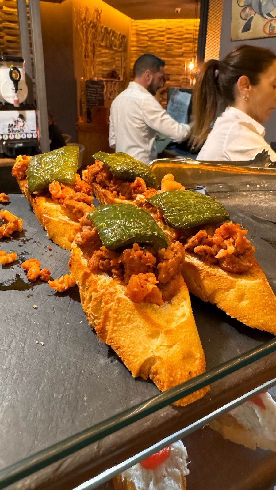 Rebanadas de pan tostado con chorizo y pimientos verdes en un mostrador de un restaurante.
