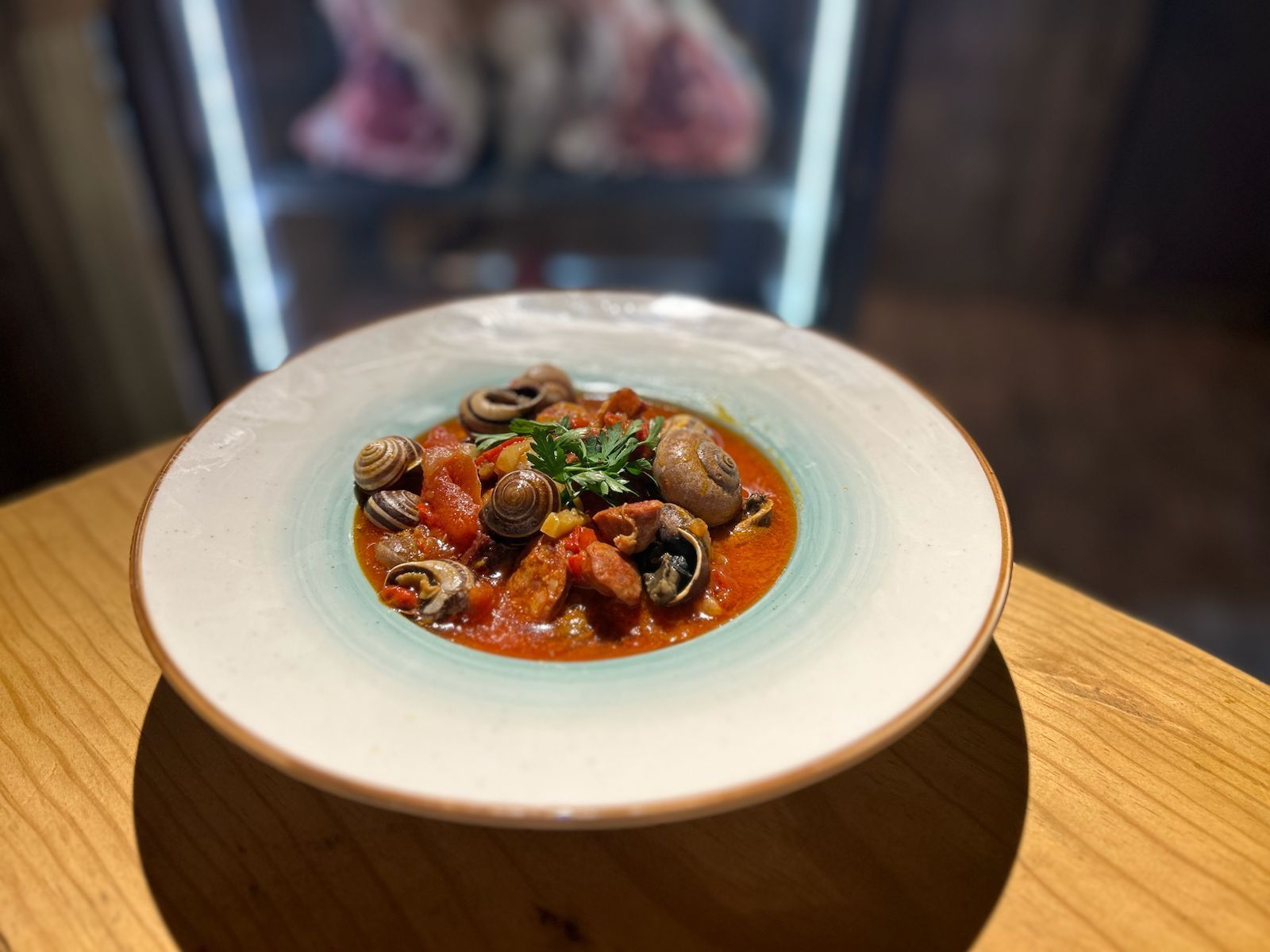 Plato de caracoles en salsa de tomate con perejil sobre una mesa de madera.