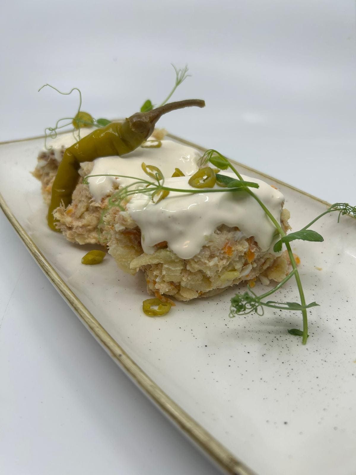 Dos porciones de comida rectangulares cubiertas con salsa blanca, un pimiento y microvegetales, en un plato rectangular.