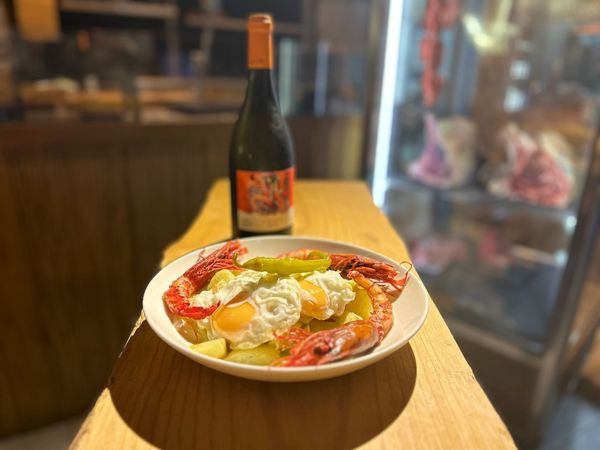 Plato de comida con huevos, pimientos y salchichas; botella de vino al fondo.