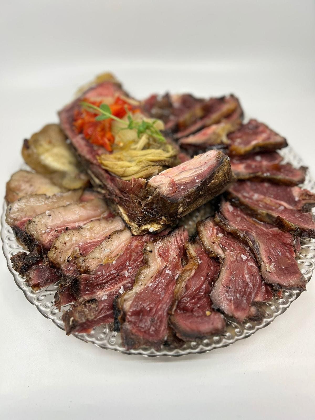 Carne asada cortada en rodajas en un plato transparente, adornada con verduras.