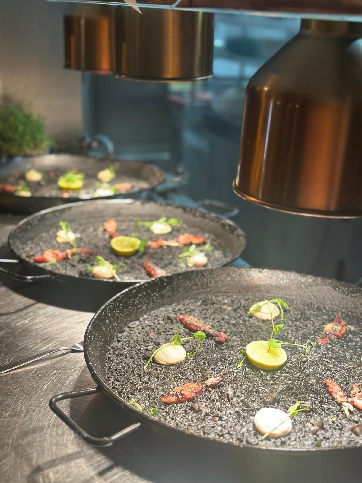 Paelleras negras con comida bajo calentadores en la cocina de un restaurante.