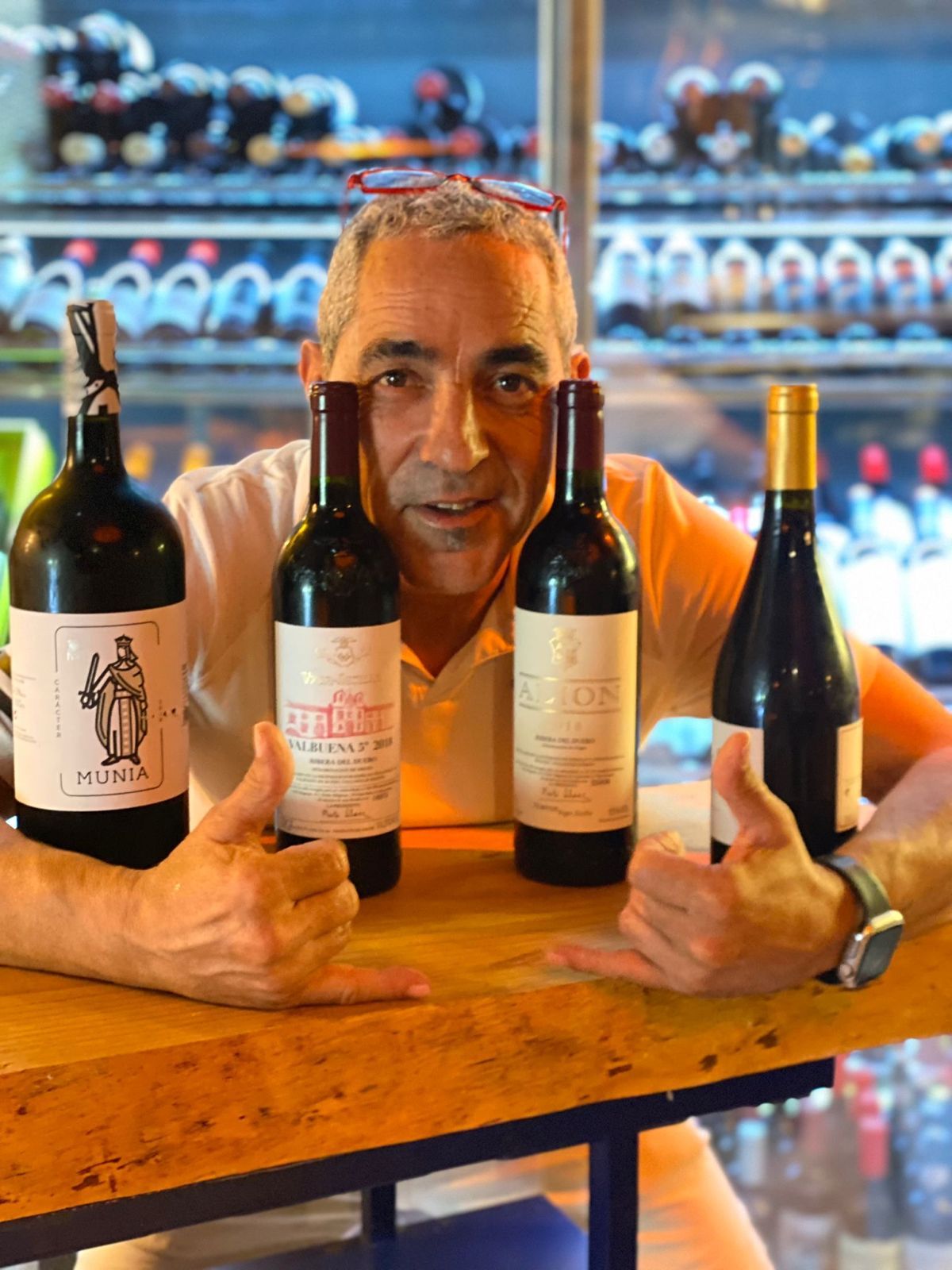 Hombre con gafas, sosteniendo cuatro botellas de vino en un bar.