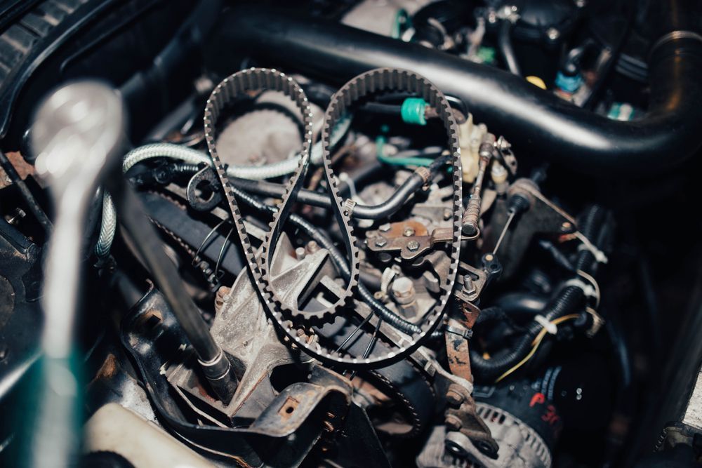 Compartimento del motor de un coche abierto que muestra la instalación o inspección de una correa de distribución, con una llave de carraca cerca.