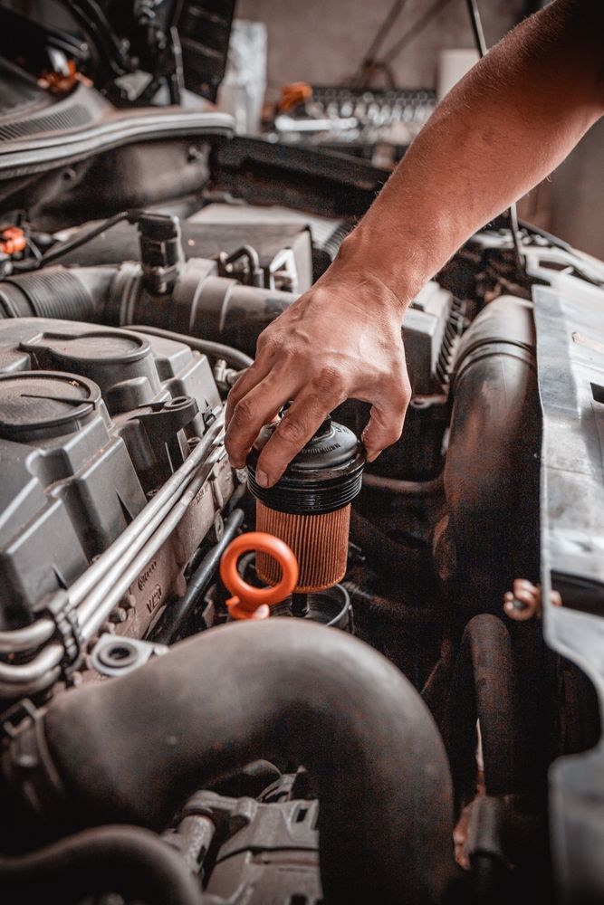 La mano de un mecánico retira un filtro de aceite cilíndrico del compartimento abierto del motor de un coche.