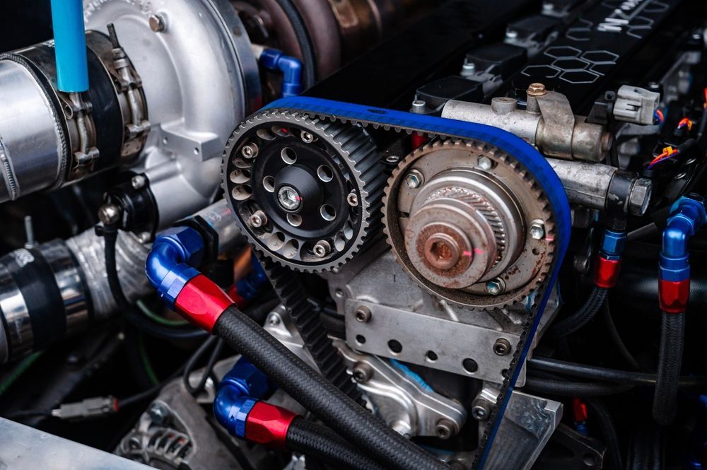 Primer plano de un motor de coche de alto rendimiento con una correa de distribución azul, engranajes metálicos y varias mangueras hidráulicas rojas y azules.
