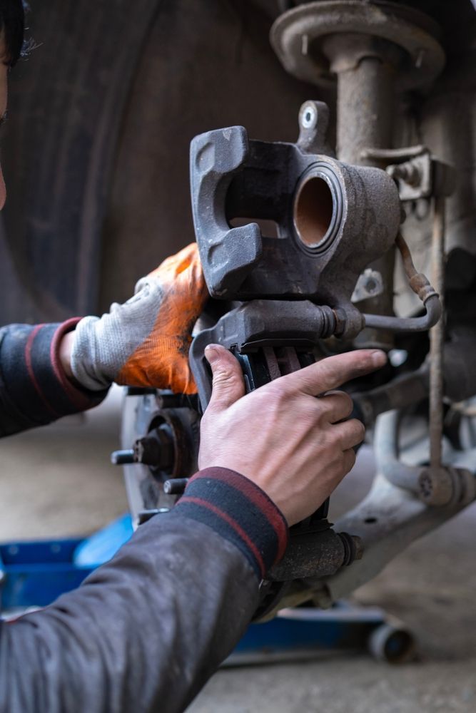 Un mecánico con un guante naranja trabaja en el conjunto de la pinza de freno de un coche en un taller.