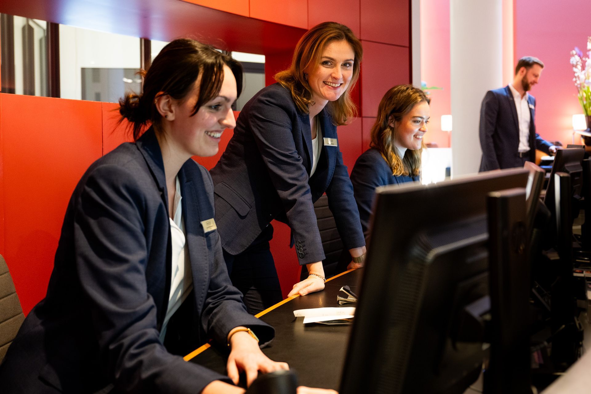 Eine Gruppe von Frauen arbeitet an einem Schreibtisch vor einem Computer an der Rezeption des THE MADISON Hotels Hamburg.