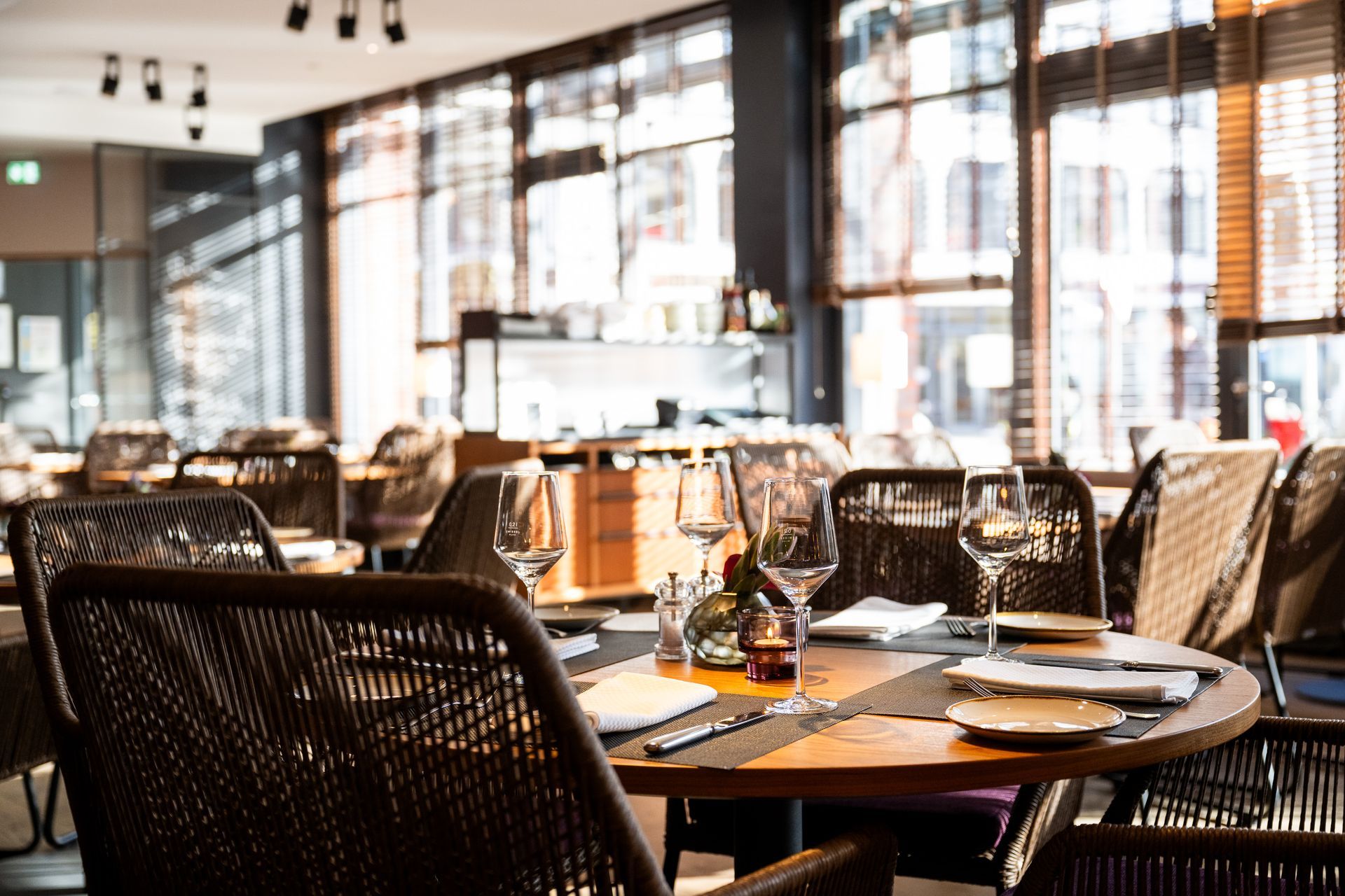 Restaurantinnenraum mit gedeckten Tischen, Sonnenlicht durch große Fenster.