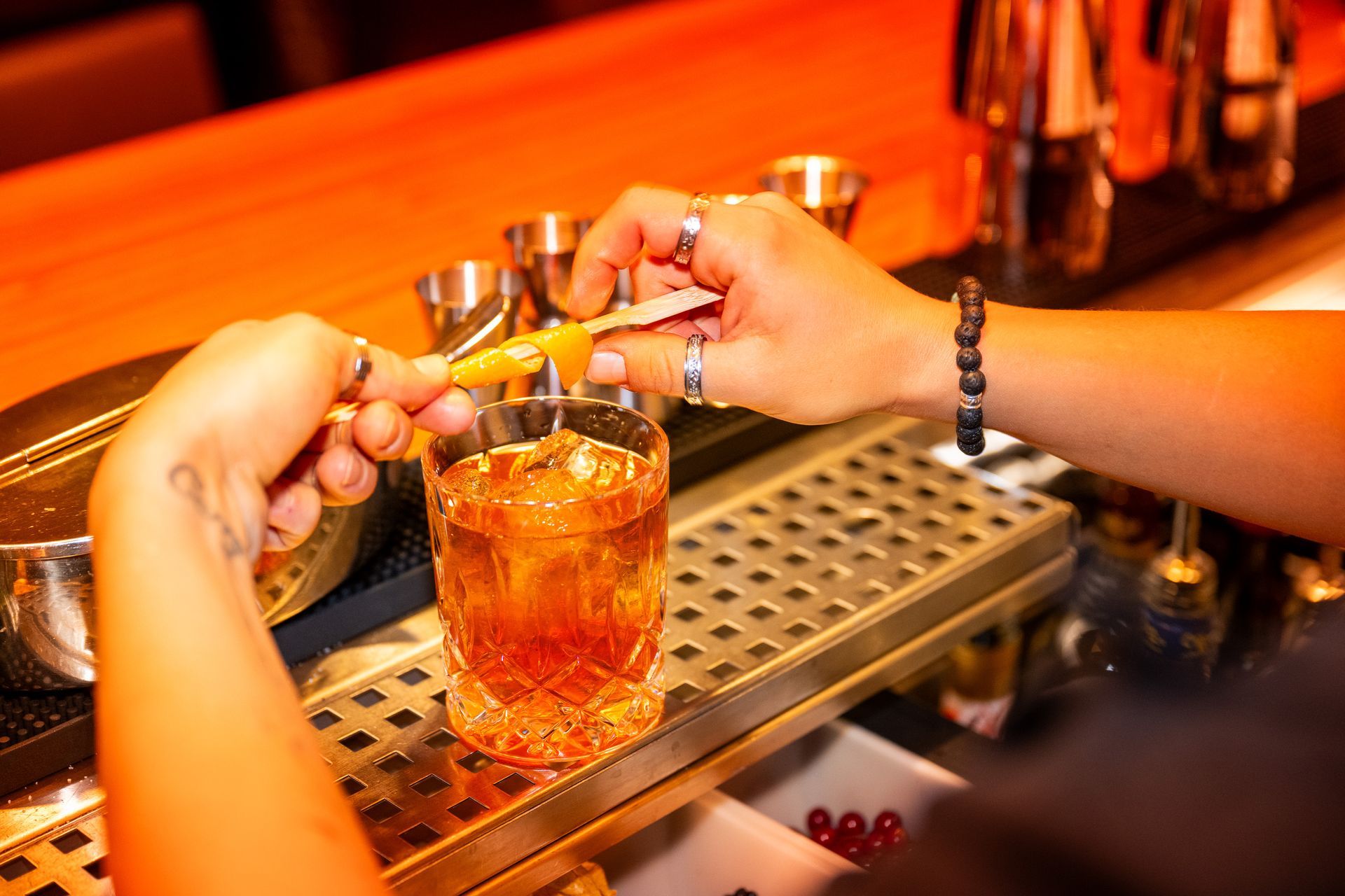 Barkeeper garniert einen Cocktail in einer Bar mit Orangenschale. Warmes, orangefarbenes Licht.
