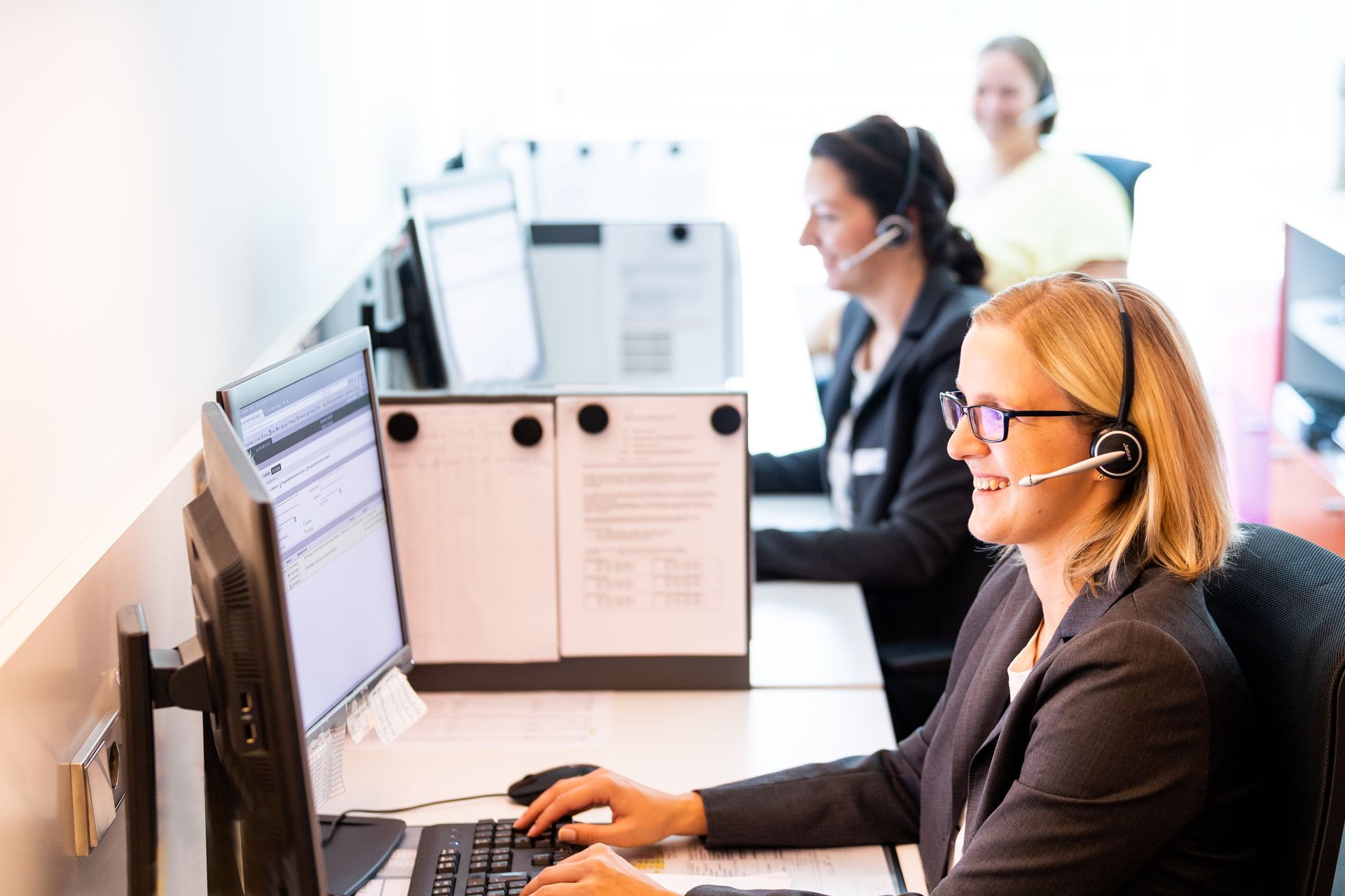 Eine Frau mit Headset sitzt an einem Schreibtisch vor einem Computer.