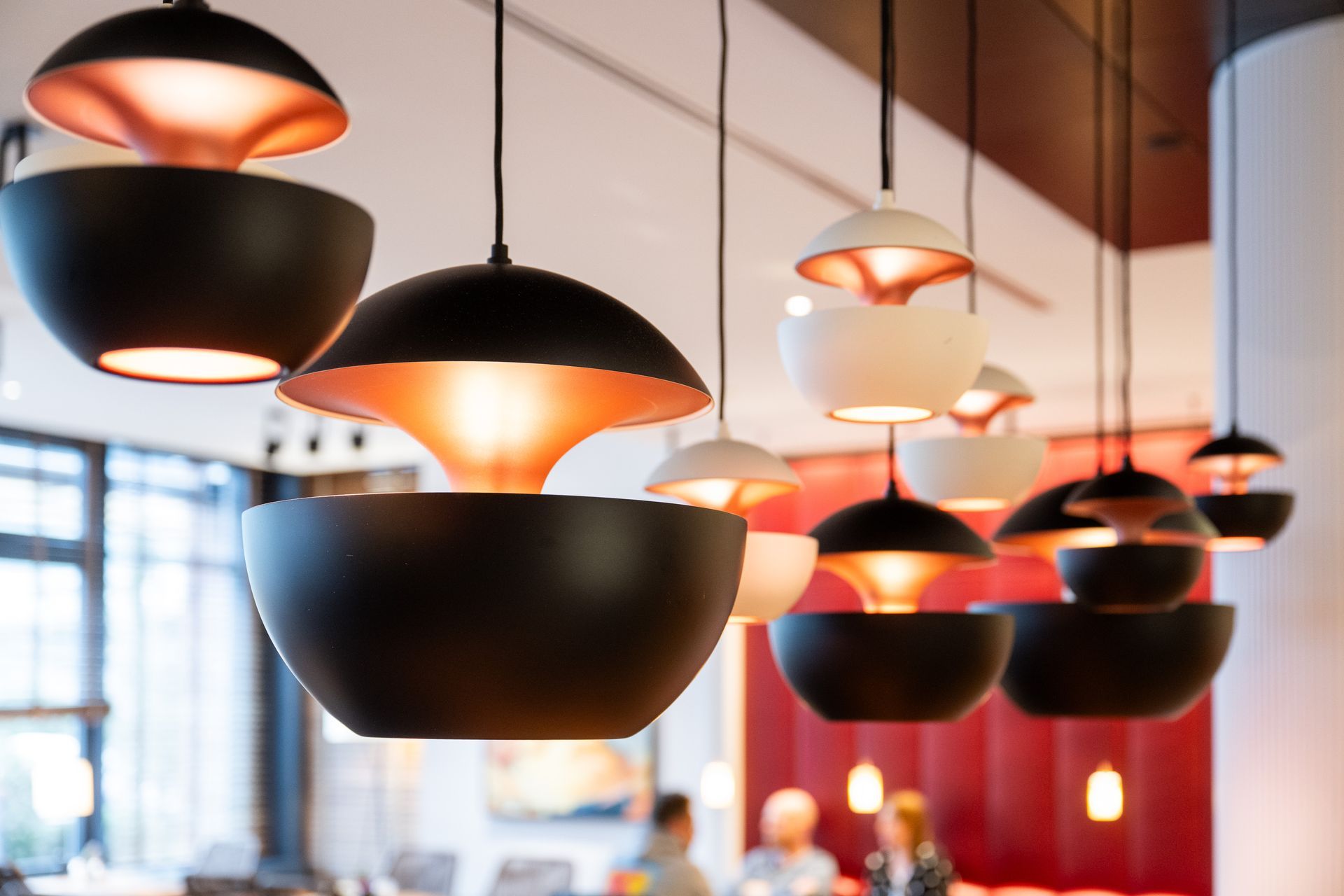 Moderne Pendelleuchten mit schwarz-weißen Schalen und Kupferinnenausstattung, hängen in einem Restaurant.