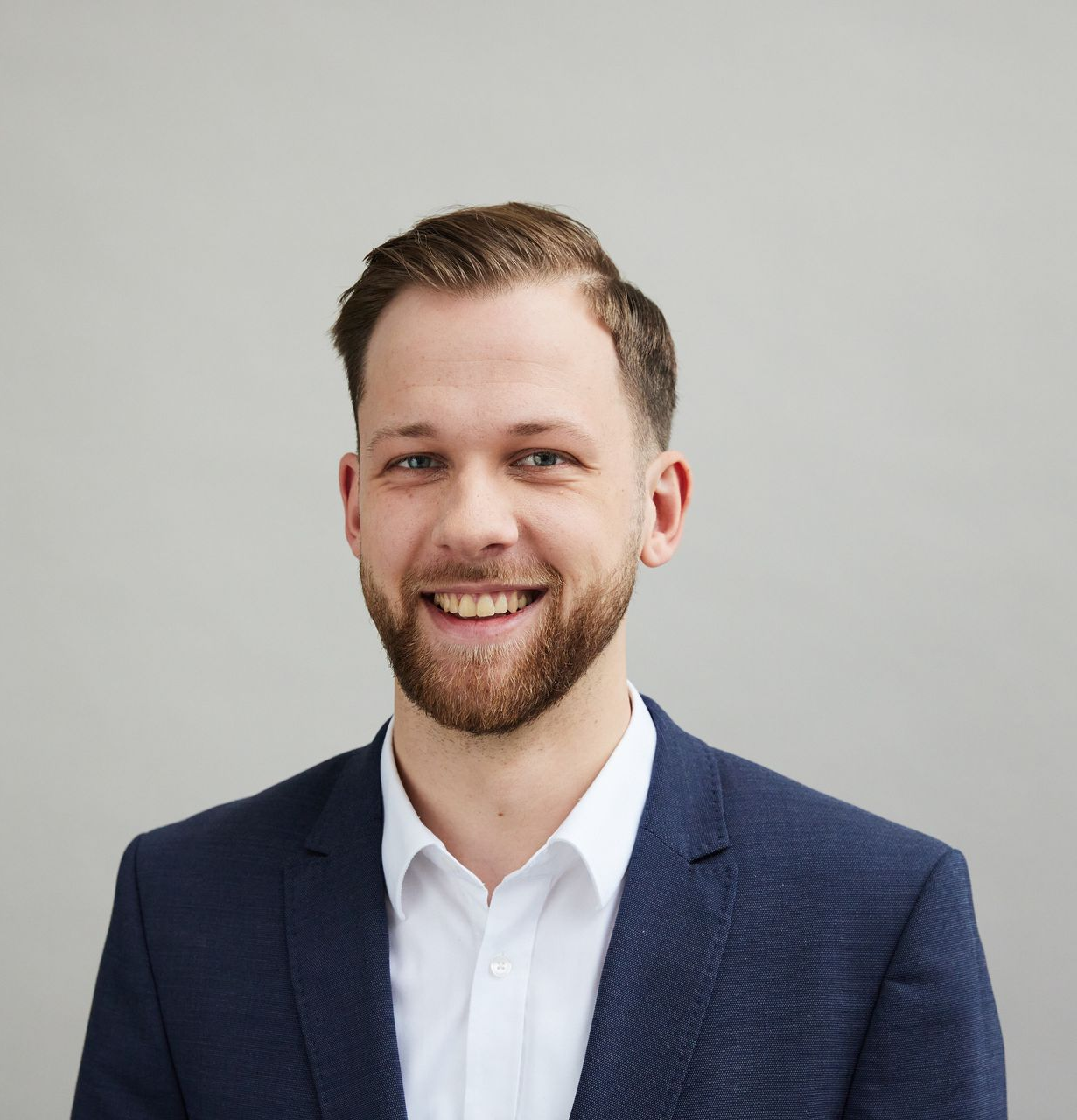 Smiling man in a navy blazer and white shirt against a light gray background