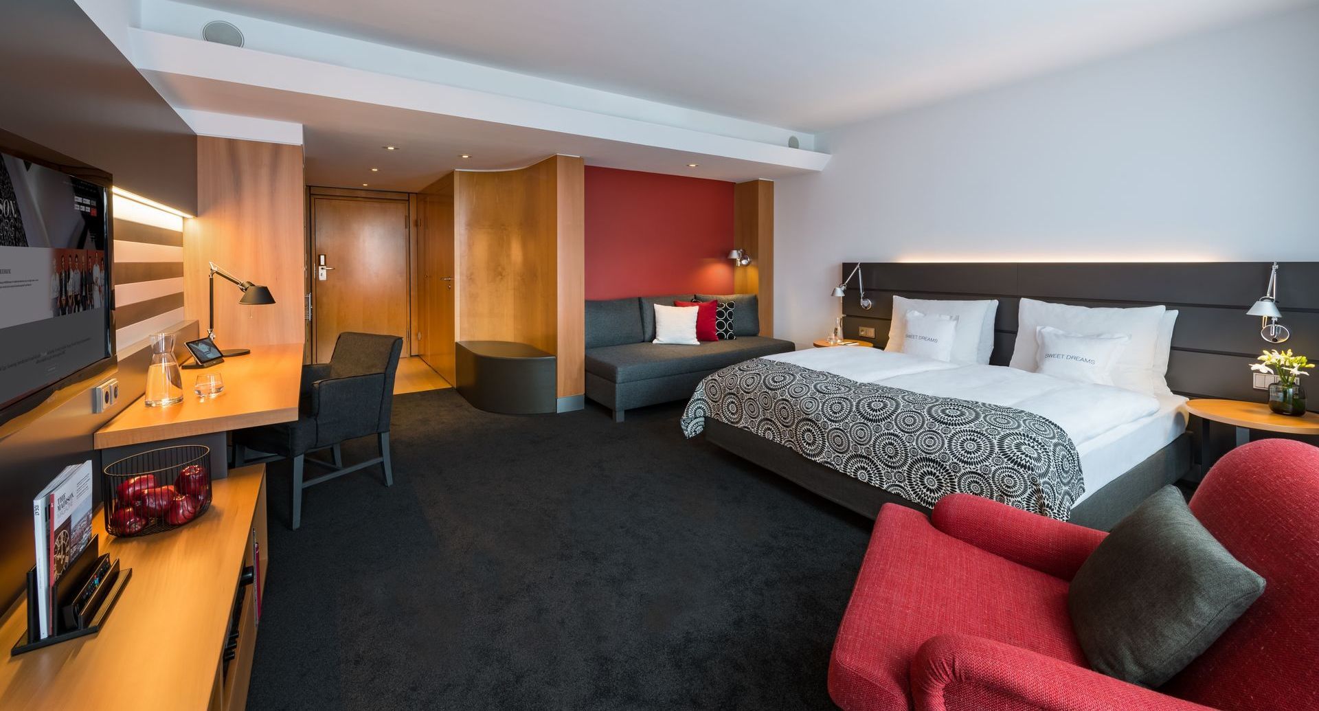 Ein Hotelzimmer mit einem großen Bett, einem roten Sessel und Fernseher im THE MADISON Hotel in Hamburg Innenstadt.