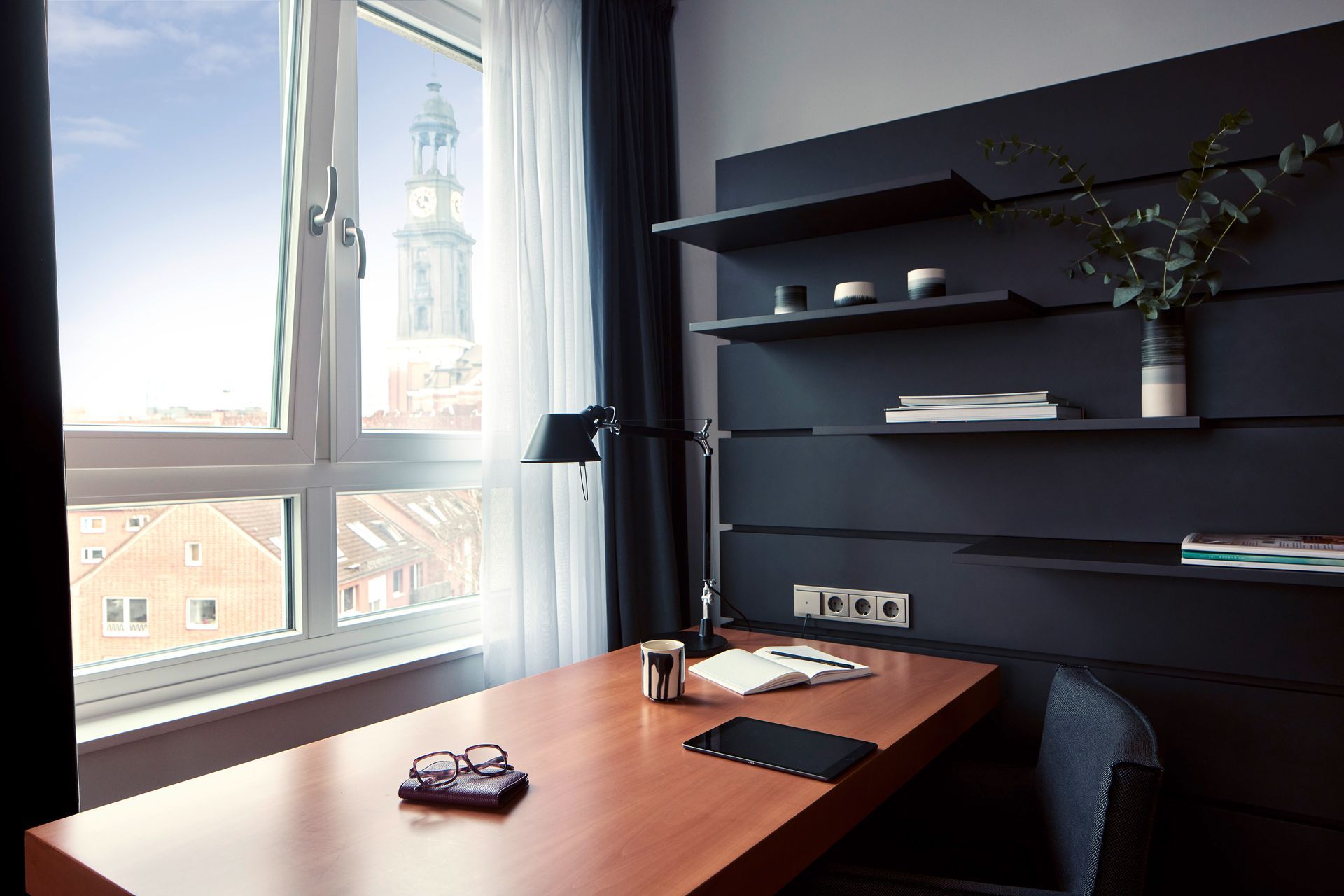 Ein Schreibtisch mit einer Lampe und einem Buch darauf in einem Raum mit einem Fenster.