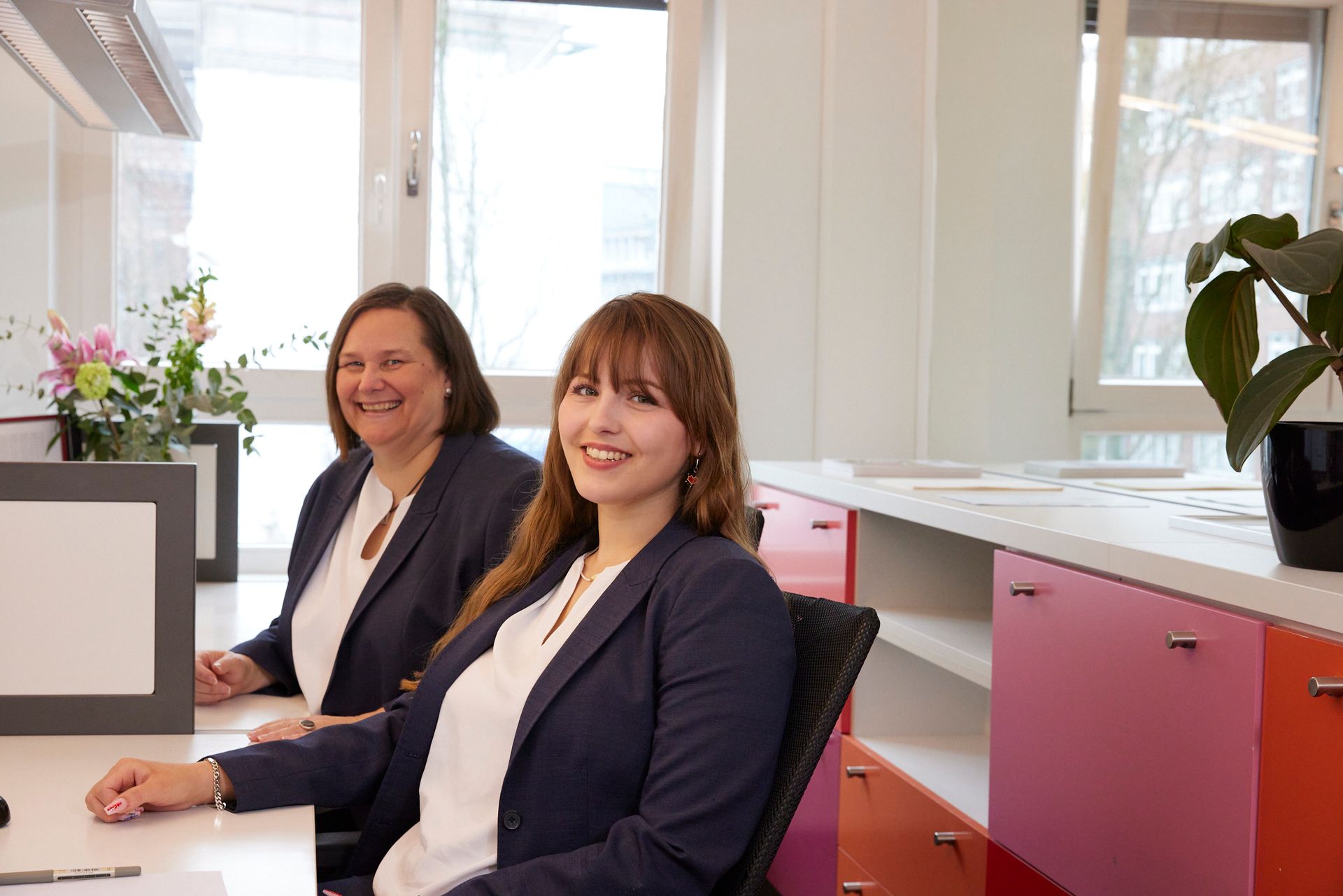 Zwei Frauen sitzen an einem Schreibtisch vor einem Computer.