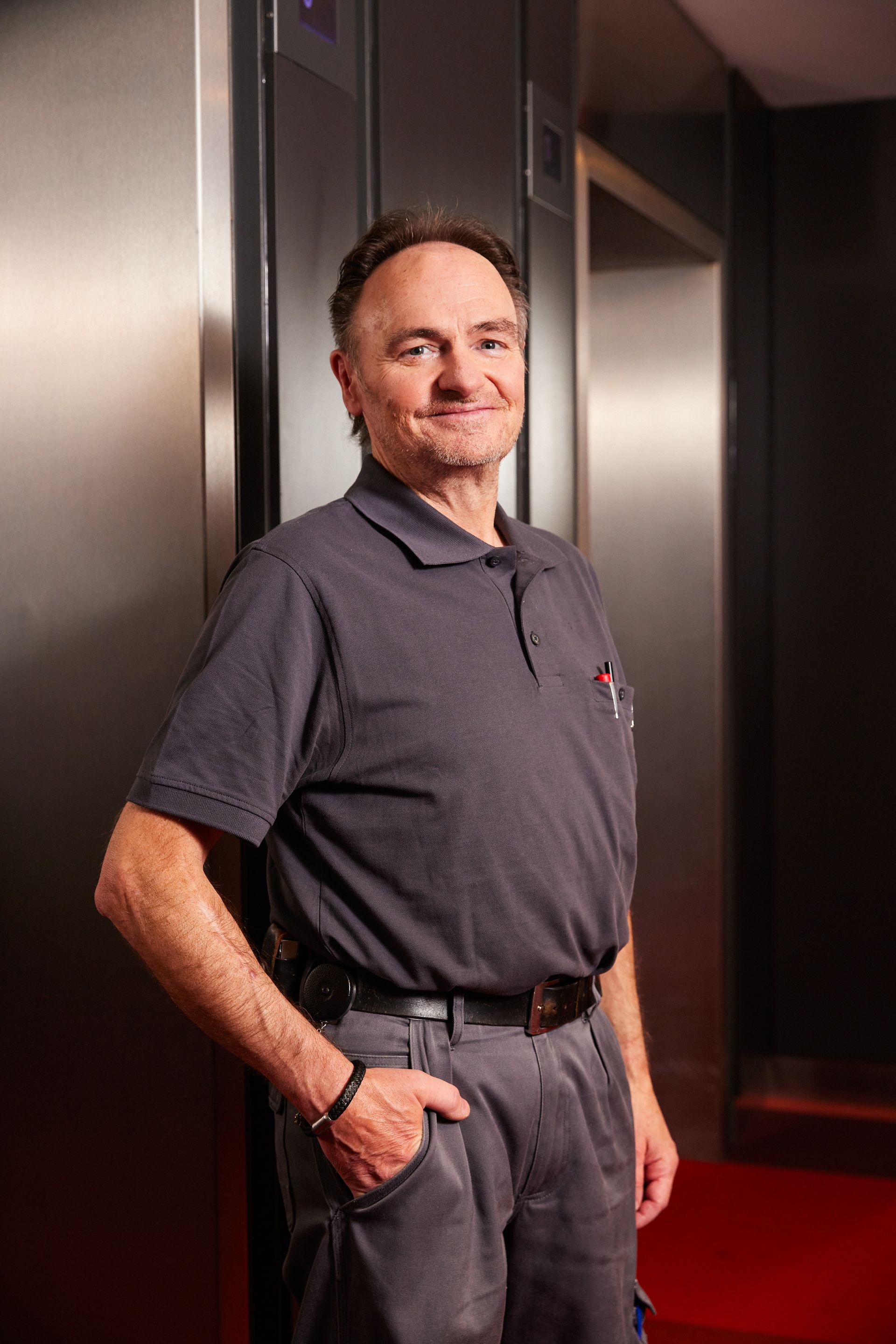 Ein Mann steht mit den Händen in den Taschen vor einem Aufzug.