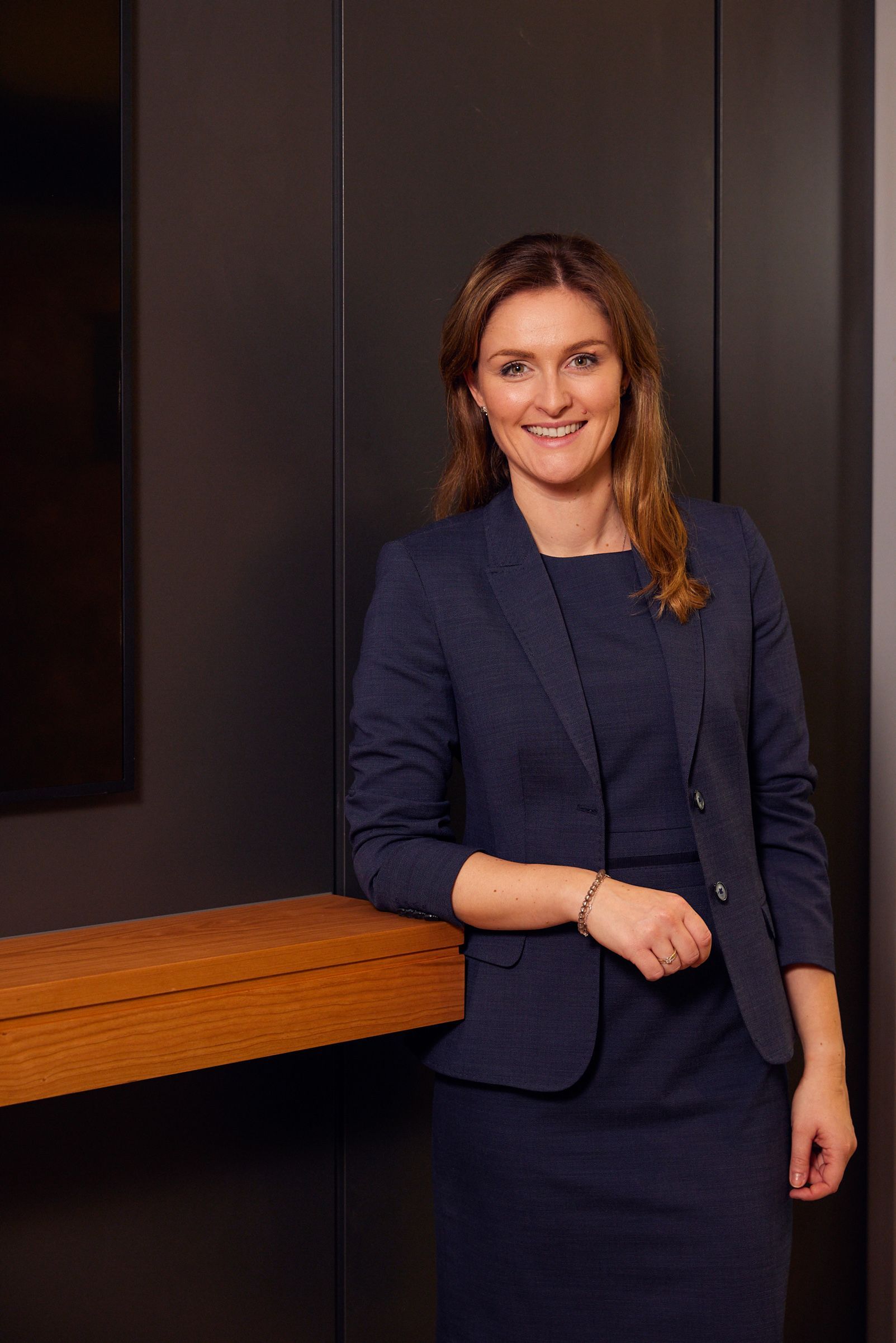 Eine Frau in einem blauen Anzug und Kleid steht neben einem Holztisch.