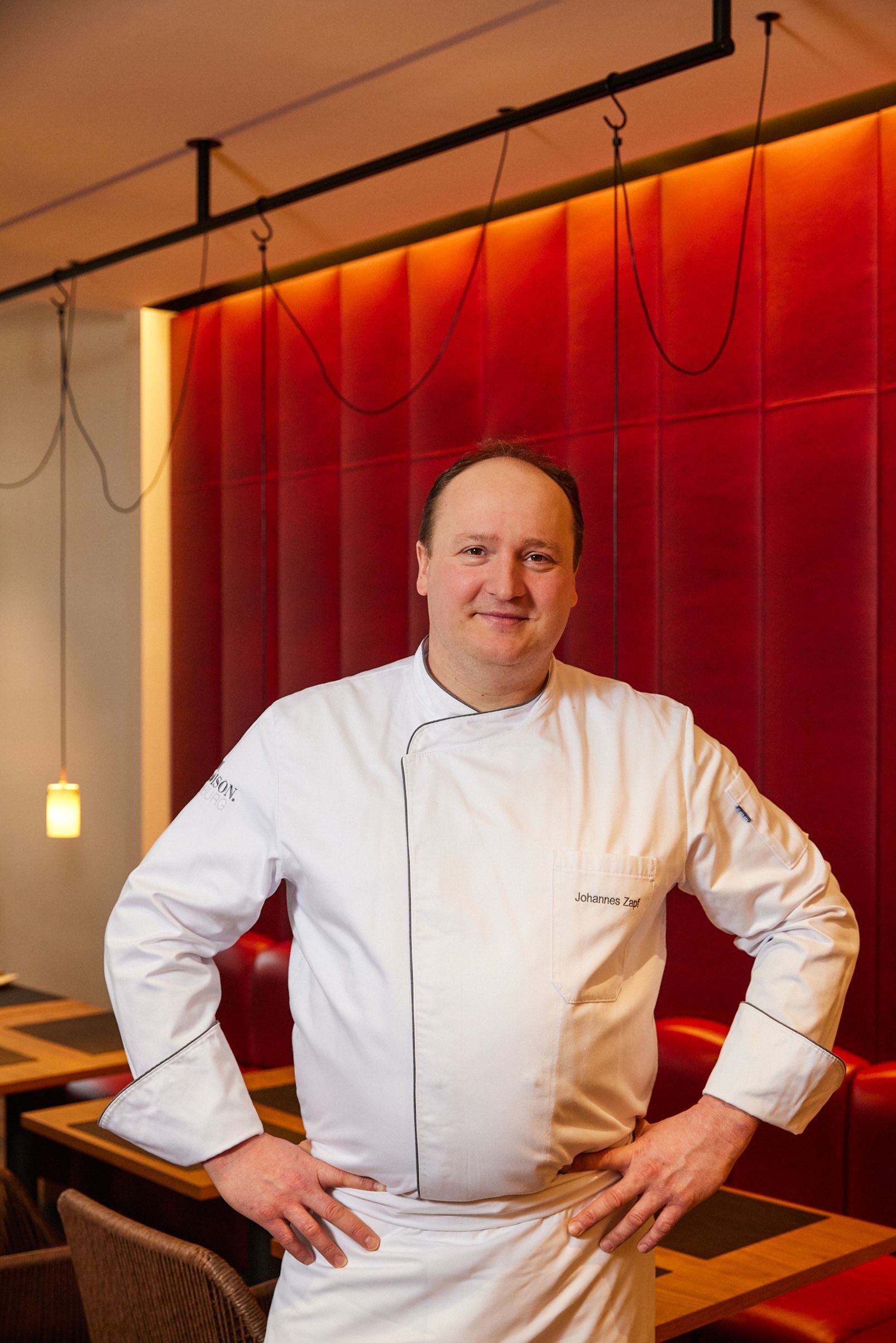 Ein Koch steht mit den Händen in den Hüften vor einer roten Wand
