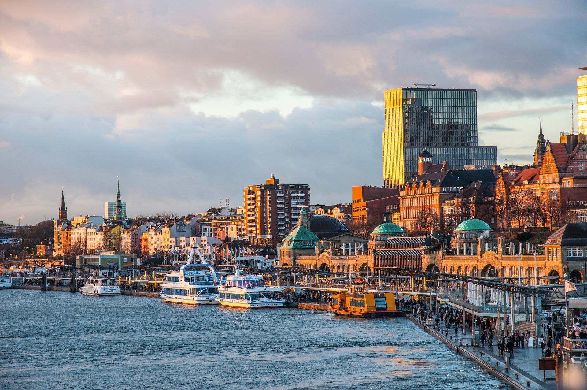 Eine Gruppe Boote liegt in einem Hafen vor Anker. Im Hintergrund ist eine Stadt zu sehen.