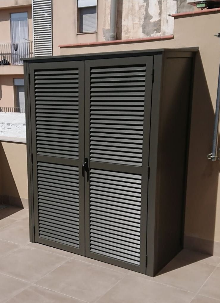 Un armario gris con persianas en las puertas está en un patio.