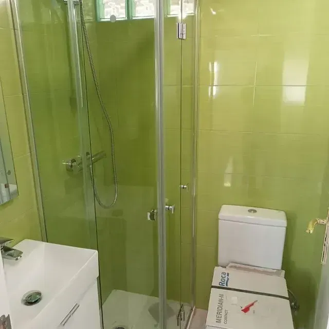 Un baño con inodoro, lavabo, ducha y azulejos verdes.