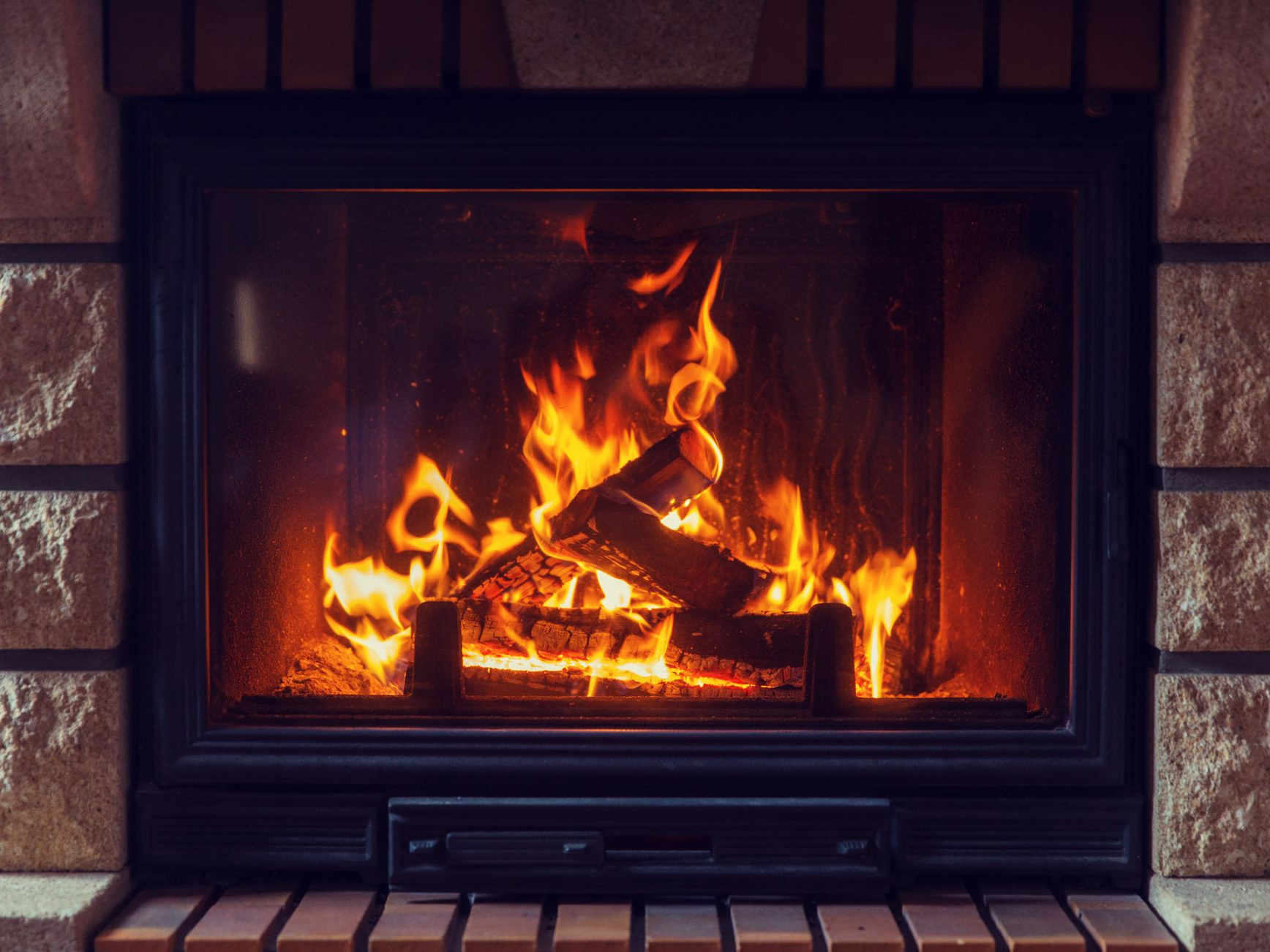 Cheminée avec bûches, flammes et entourage en briques.