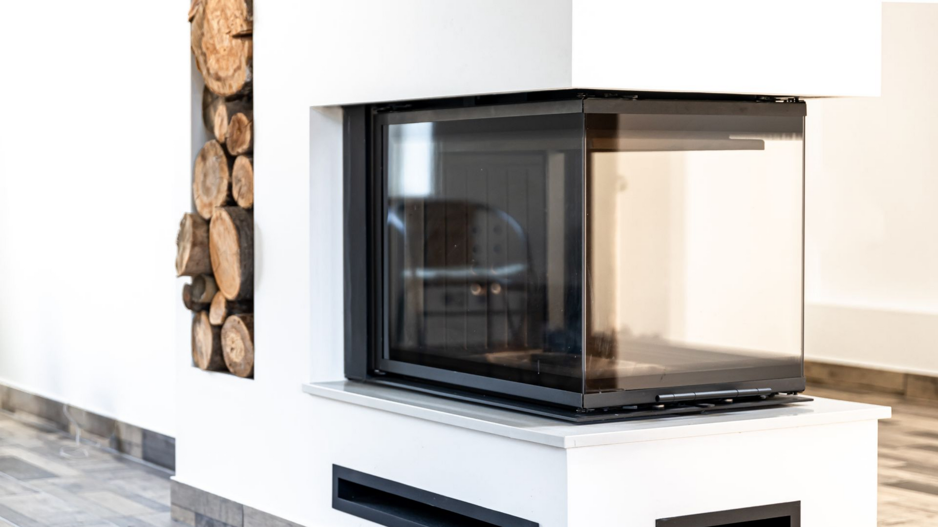 Cheminée moderne avec cadre et vitre noirs, encastrée dans un mur blanc et un espace de rangement pour le bois de chauffage.