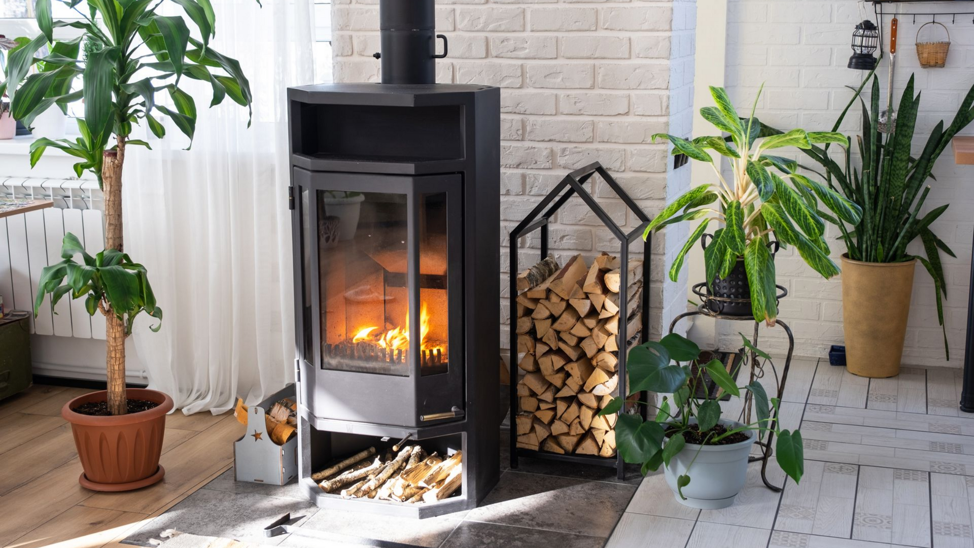 Cheminée avec flammes, rangement pour le bois et plantes en pot dans une pièce lumineuse.