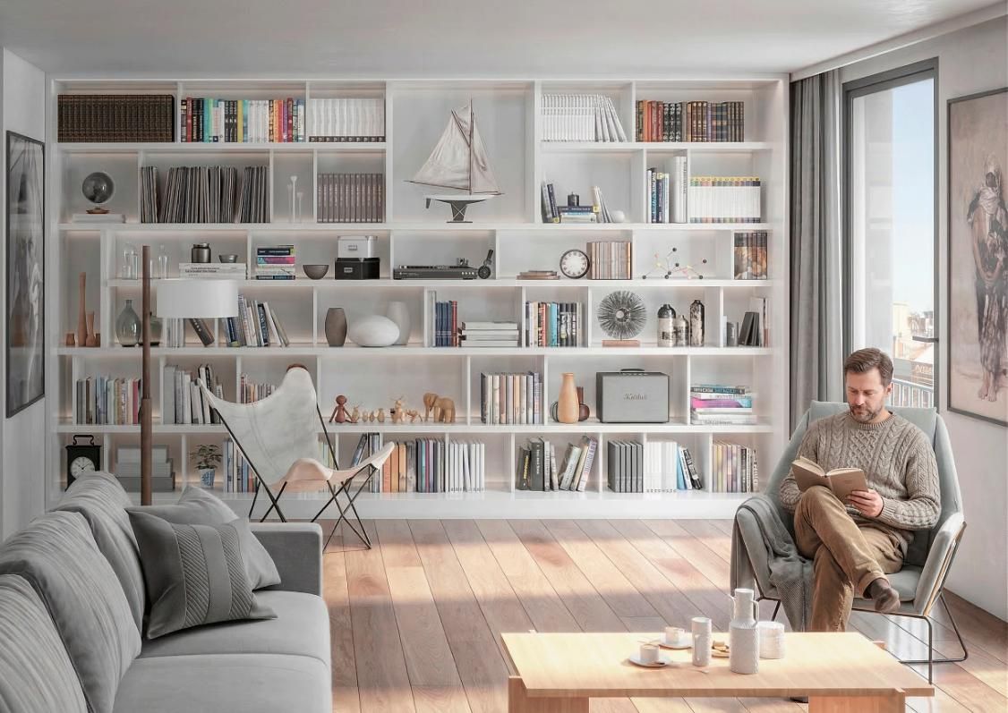 Una persona está sentada en un sillón leyendo un libro en una sala de estar soleada con una gran estantería blanca 