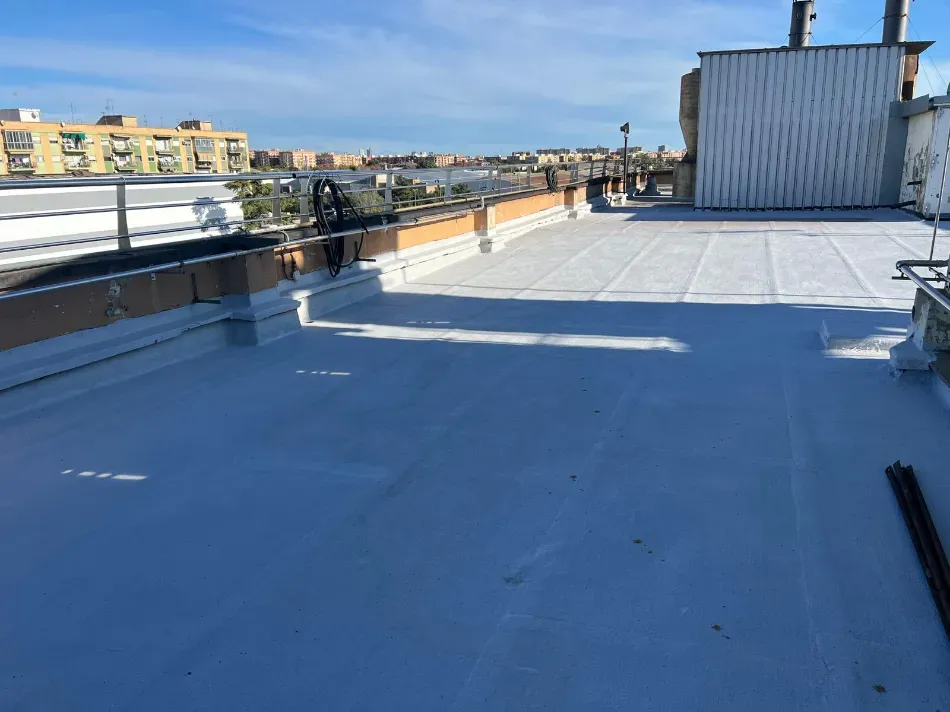 Azotea plana azul con rejillas de ventilación y el perfil de la ciudad a lo lejos bajo un cielo despejado.