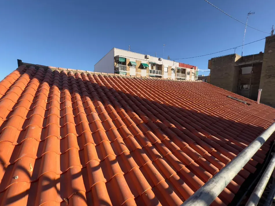Azotea con tejas de terracota naranja bajo un cielo azul claro, con edificios de apartamentos al fondo.