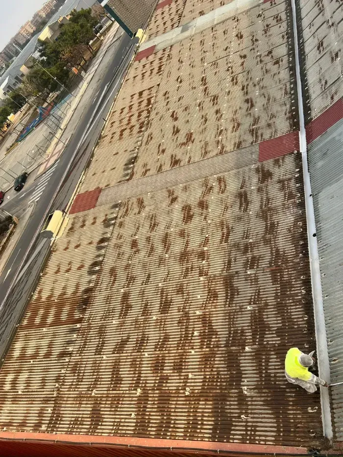 Azotea con chapa ondulada manchada de óxido y un trabajador con un chaleco de seguridad amarillo cerca del borde.