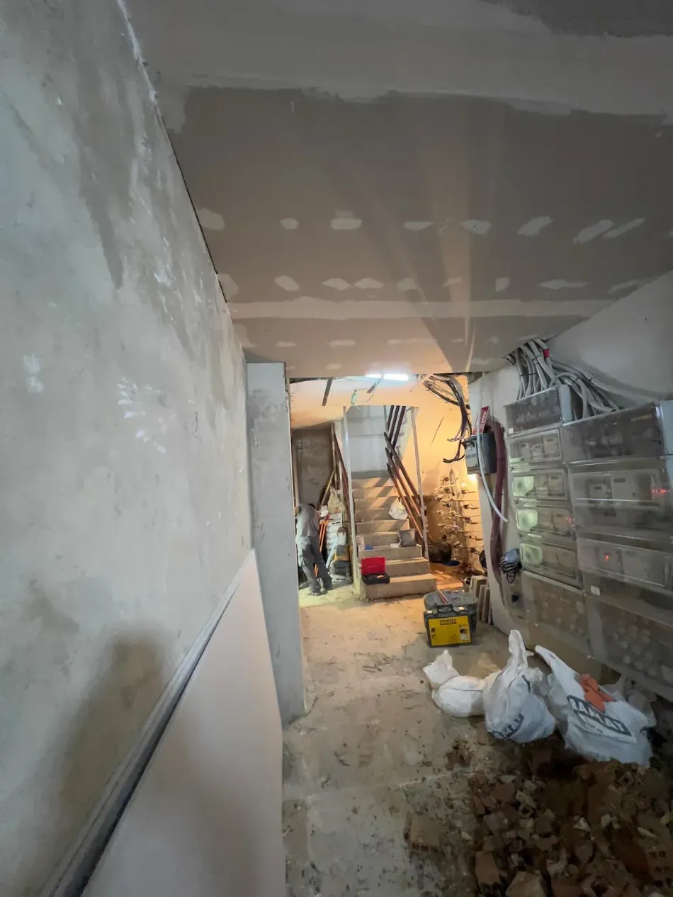 Pasillo estrecho y sin terminar con materiales de construcción, escaleras y escombros bajo un techo remendado.