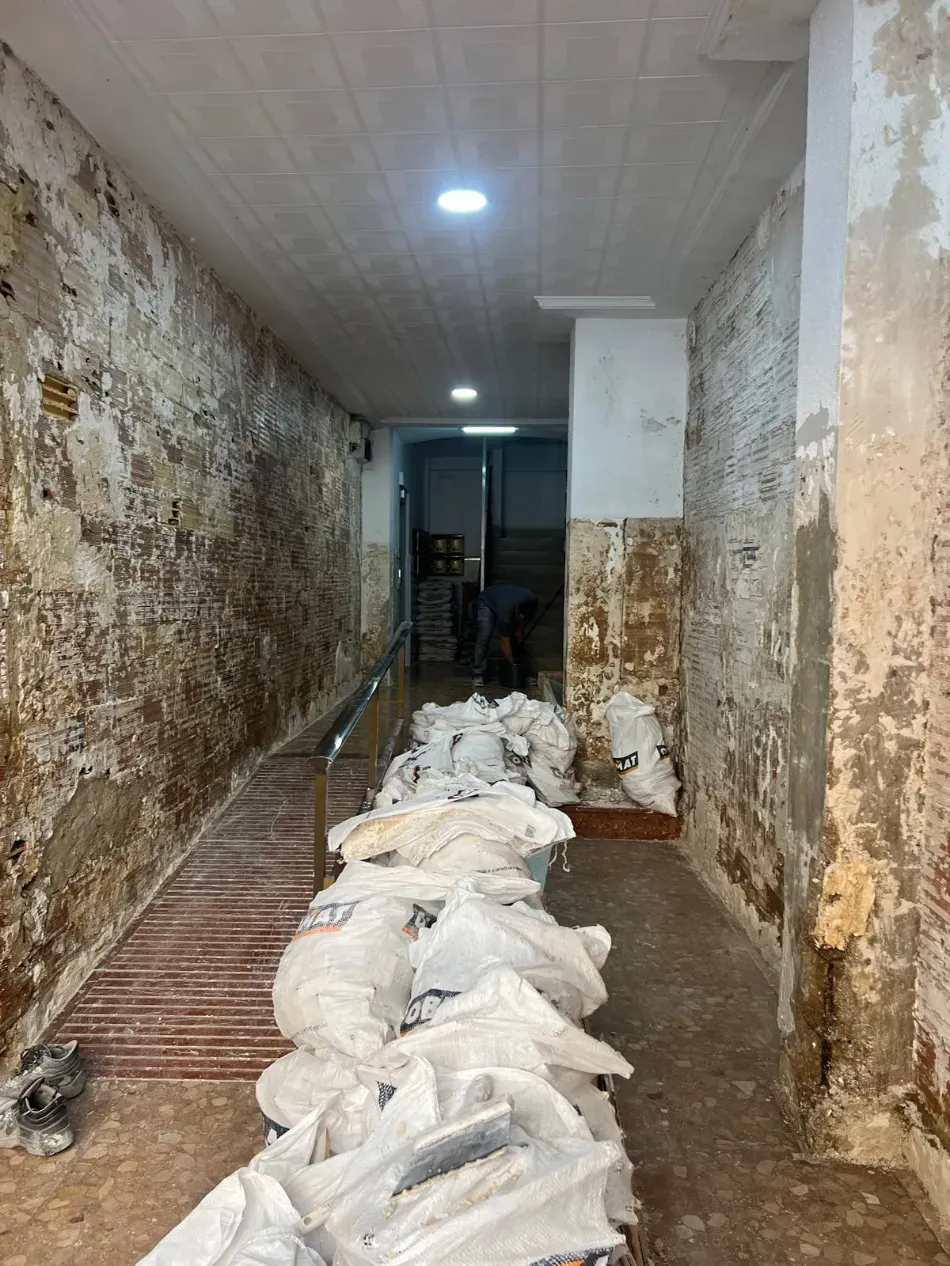 Un estrecho pasillo interior con paredes desconchadas y una larga pila de sacos blancos en el suelo.