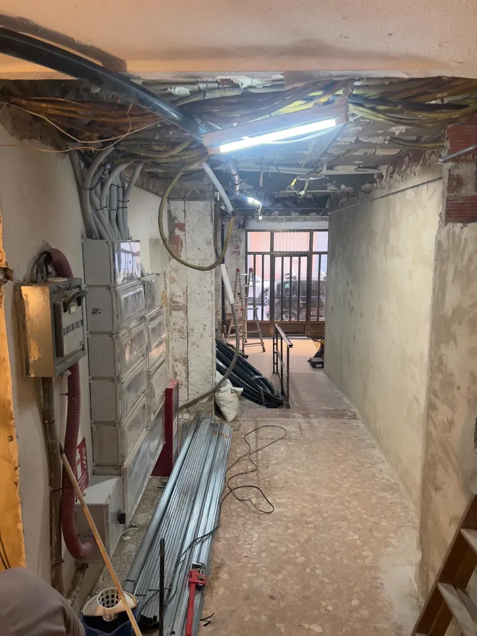 Pasillo estrecho y sin terminar, con cables a la vista, materiales de construcción y una luz brillante en el techo.