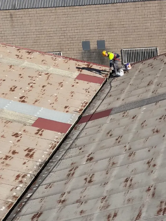 Un trabajador con casco amarillo repara un tejado inclinado cerca del borde de un edificio.