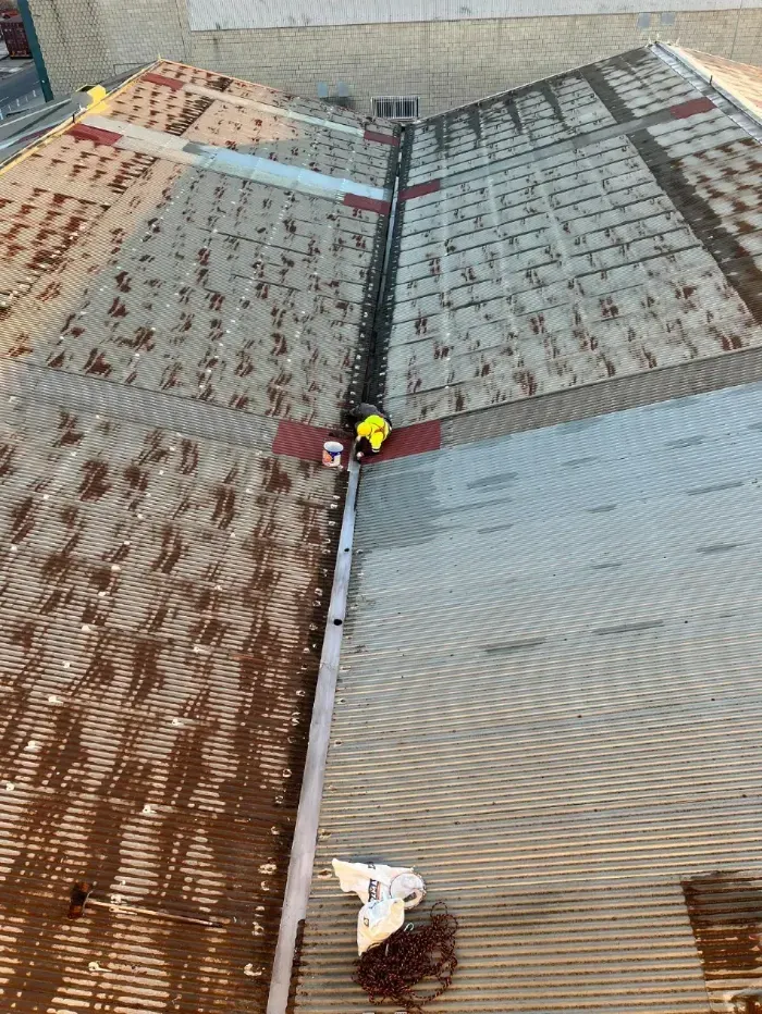 Trabajadores en un tejado de metal oxidado, sujetos con cuerdas durante las labores de mantenimiento.