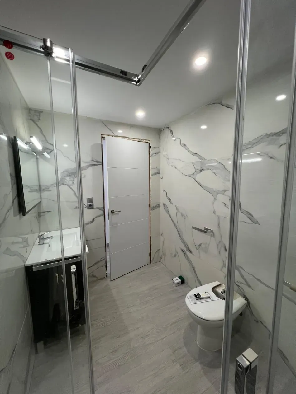 Baño moderno con paredes de mármol, ducha de cristal, lavabo mural e inodoro.