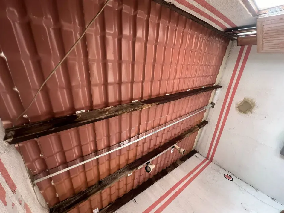 Techo interior con paneles corrugados rojos, vigas a la vista y paredes blancas con rayas rojas.