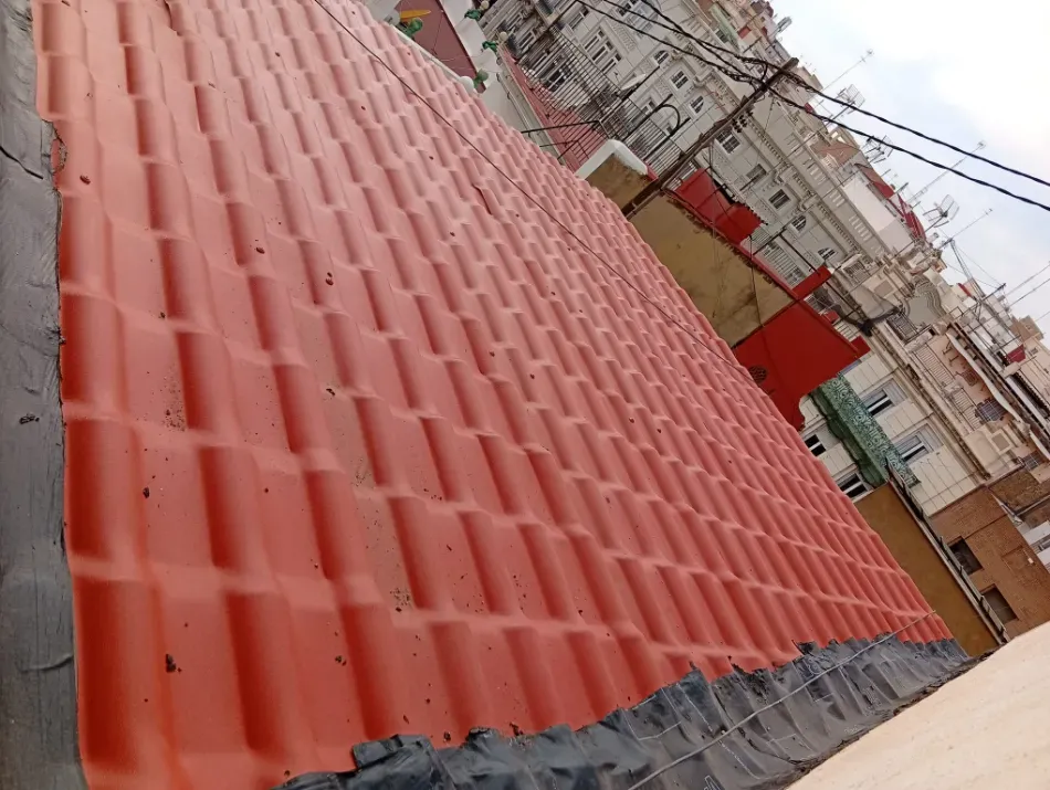 Techo de chapa ondulada roja con un trozo de lona gris en un barrio urbano.