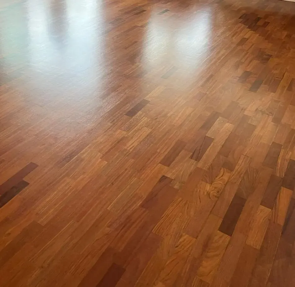 Suelo de madera noble pulida con reflejos de luz en una habitación prácticamente vacía.