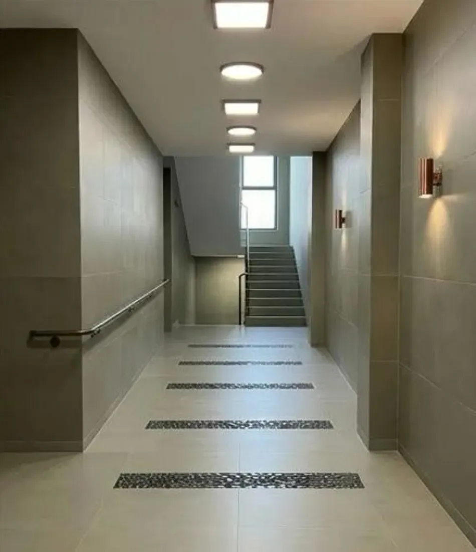 Pasillo vacío con escaleras al final, paredes grises y luces en el techo.