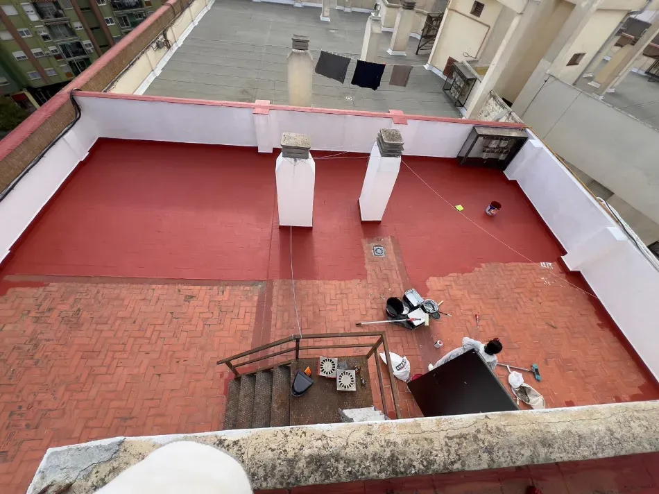 Terraza en la azotea con suelo rojo, paredes blancas y dos chimeneas, vista desde arriba.