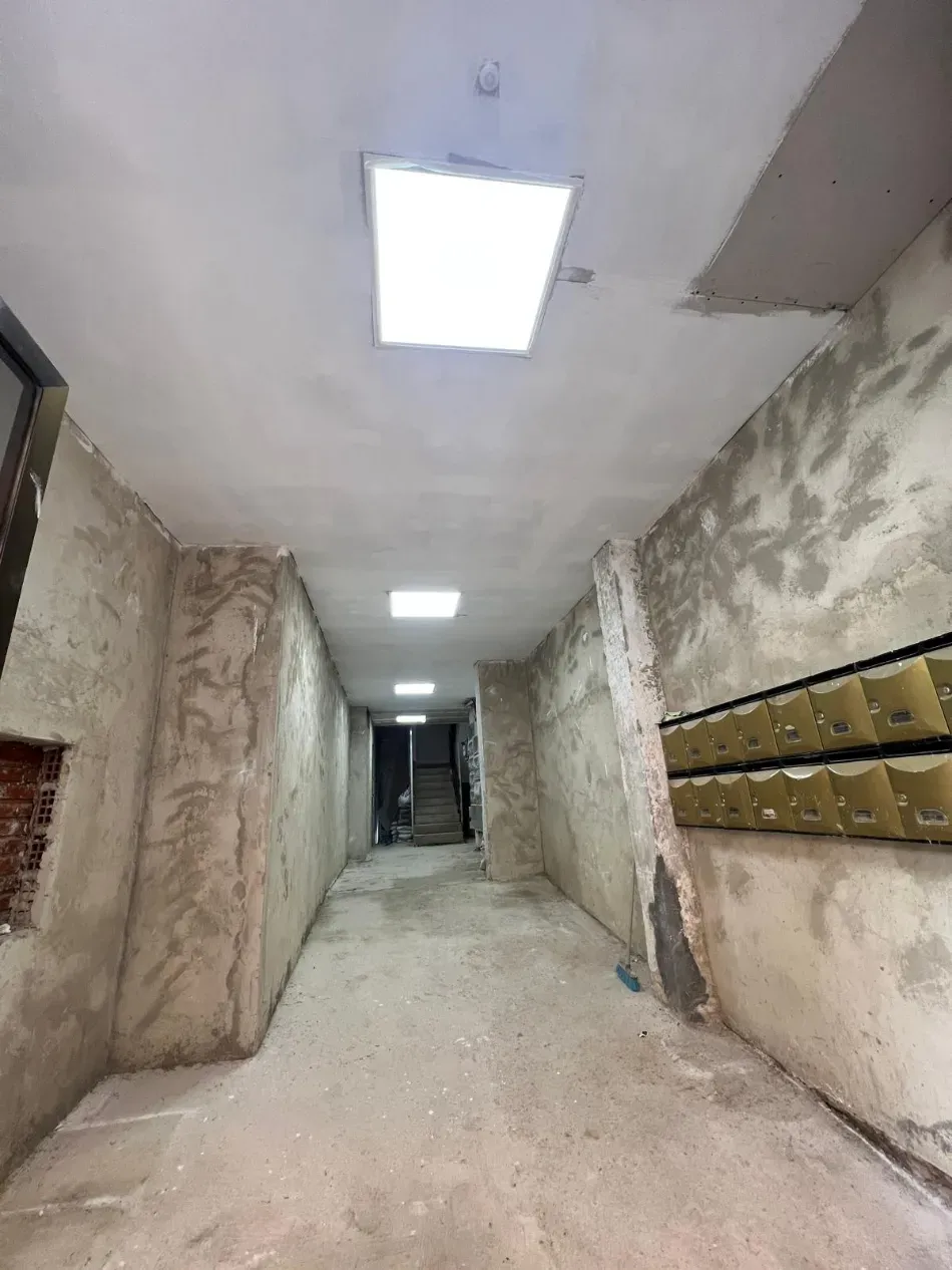 Pasillo estrecho sin terminar con paredes de yeso rugoso y luces en el techo.